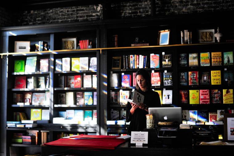 Inside a bookshop at night with tall shelves and readers browsing
